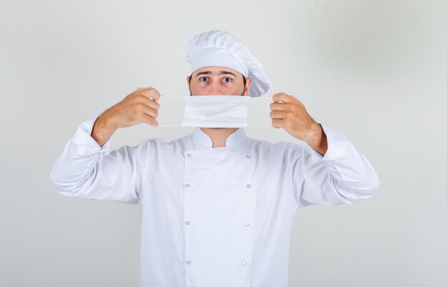 Chef masculino en uniforme blanco con máscara médica sobre la boca