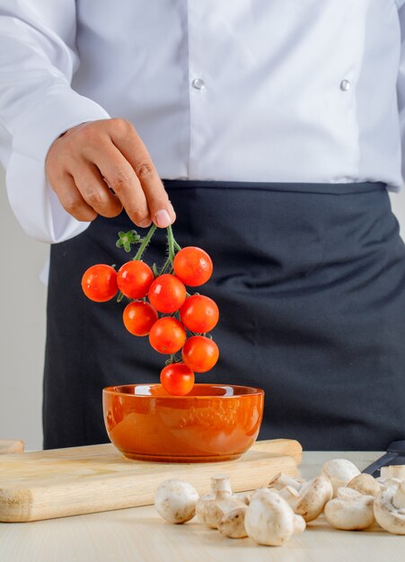 Chef masculino en uniforme y delantal sacando tomates del tazón en la cocina