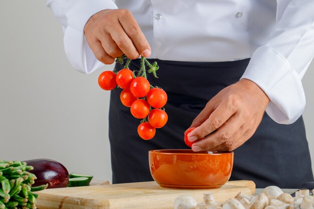 Chef masculino en uniforme y delantal sacando tomates del tazón en la cocina