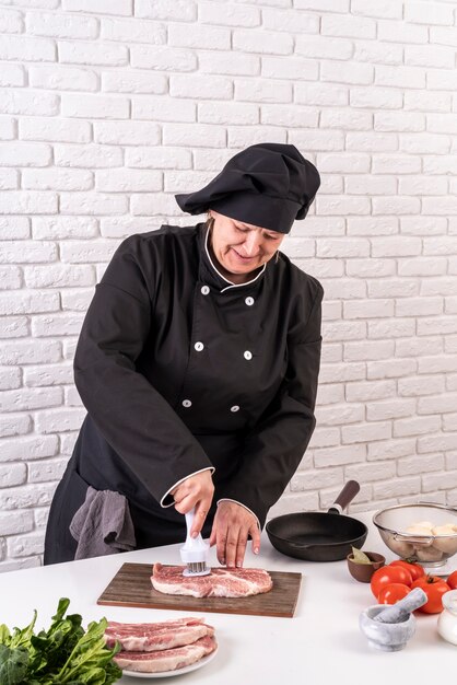 Chef mujer ablandando la carne en la cocina