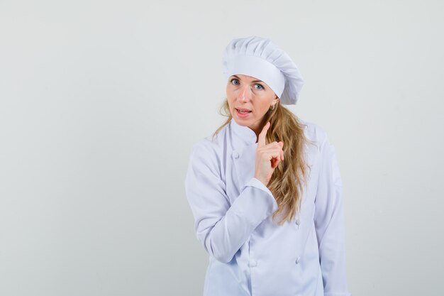 Chef mujer en advertencia uniforme blanco con el dedo hacia arriba y mirando serio