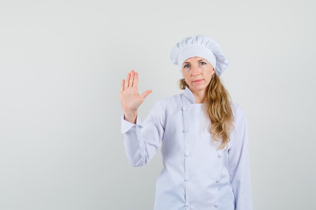 Chef mujer agitando la mano para decir adiós en uniforme blanco y mirando tranquila