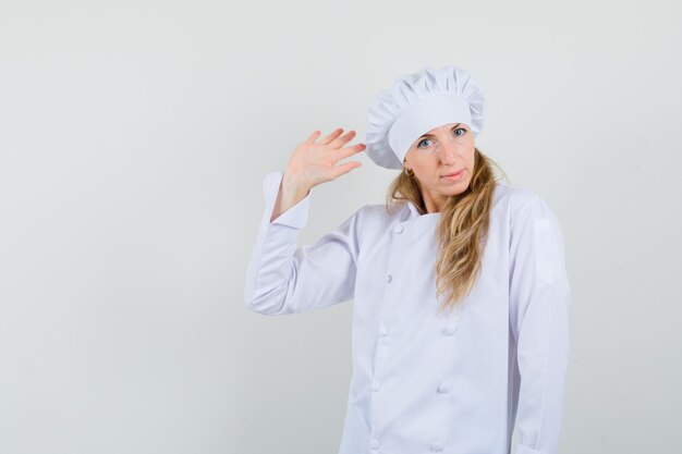 Chef mujer agitando la mano para saludar en uniforme blanco y mirando positivo.