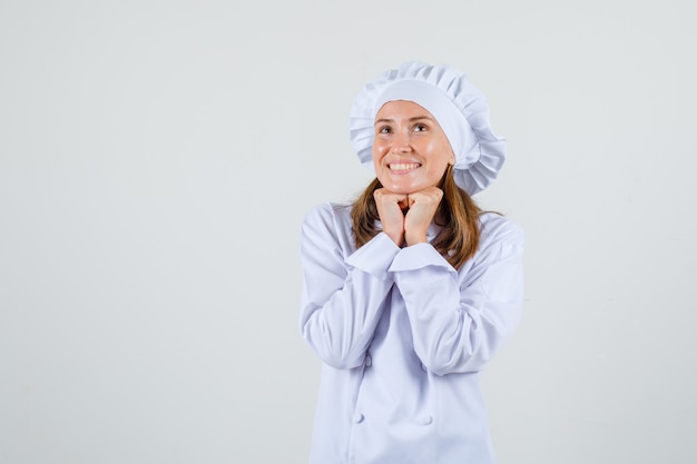 Chef mujer apoyando la barbilla en los puños en uniforme blanco y mirando esperanzado