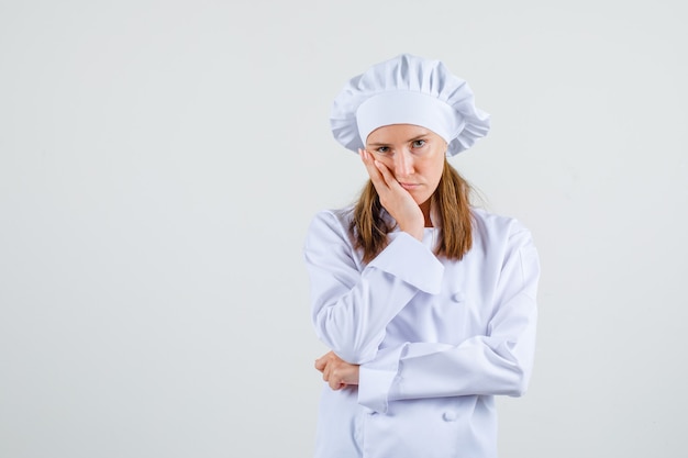 Chef mujer apoyándose en la mejilla de la palma levantada en uniforme blanco y mirando triste