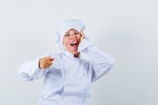 Chef mujer apuntando al frente, sosteniendo la mano en la mejilla en uniforme blanco