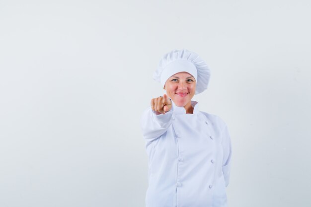 Chef mujer apuntando al frente con uniforme blanco y mirando contento