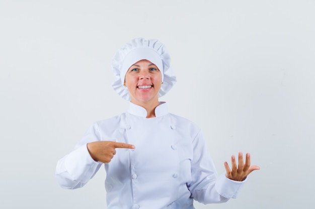 Chef mujer apuntando a algo que pretendía ser retenido en uniforme blanco y mirando confiado