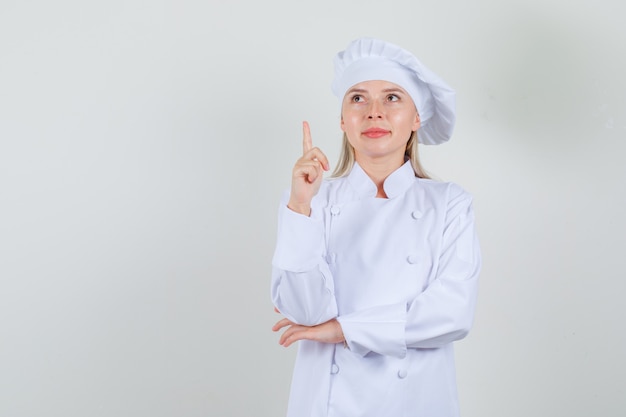 Chef mujer apuntando hacia arriba con el dedo y sonriendo en uniforme blanco