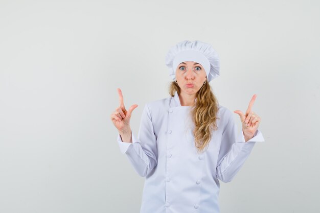 Chef mujer apuntando hacia arriba en uniforme blanco y mirando asustado