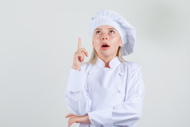 Chef mujer apuntando con el dedo hacia arriba en uniforme blanco y mirando enfocado