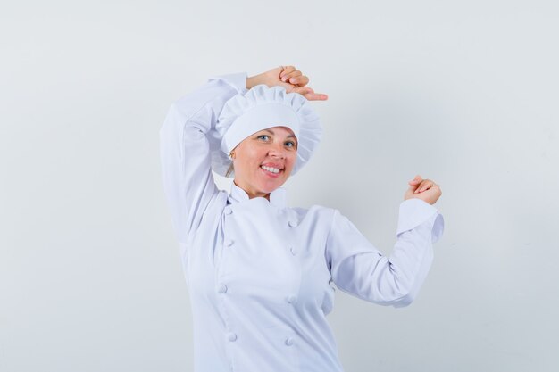 Chef mujer apuntando a un lado en uniforme blanco y mirando feliz