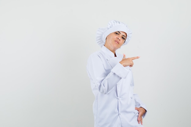 Chef mujer apuntando hacia el lado en uniforme blanco y mirando seria.