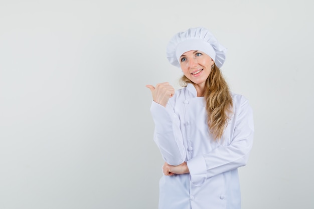 Chef mujer apuntando el pulgar hacia arriba en uniforme blanco y mirando feliz.