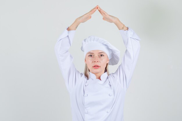 Chef mujer cogidos de la mano sobre la cabeza como techo de la casa en uniforme blanco