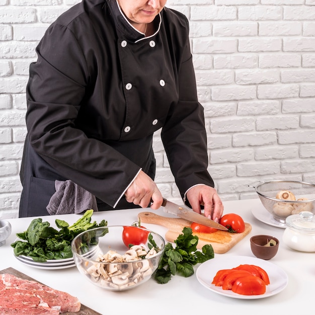 Chef mujer cortando tomates para plato