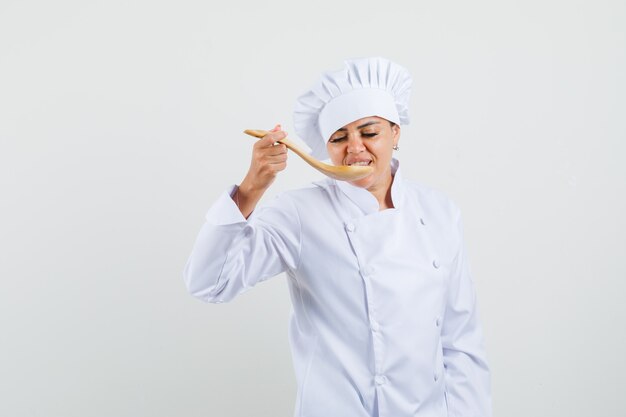 Chef mujer degustación de comida con cuchara de madera en uniforme blanco