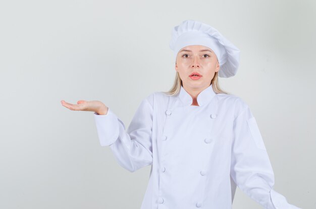 Chef mujer gesticulando como sosteniendo algo en uniforme blanco y mirando confundido