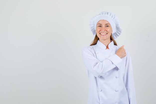 Chef mujer gesticulando con el puño cerrado en uniforme blanco y mirando alegre