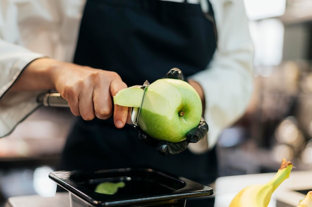 Chef mujer con guante y delantal quitando piel de manzana