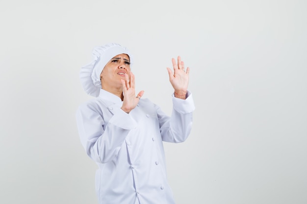 Chef mujer levantando las palmas para defenderse en uniforme blanco y mirando asustada.