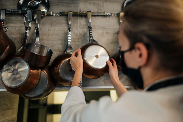 Chef mujer con máscara eligiendo sartén para cocinar