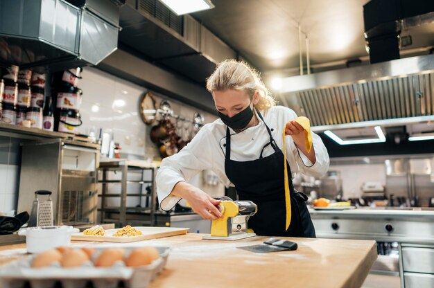 Chef mujer con máscara rodando masa de pasta