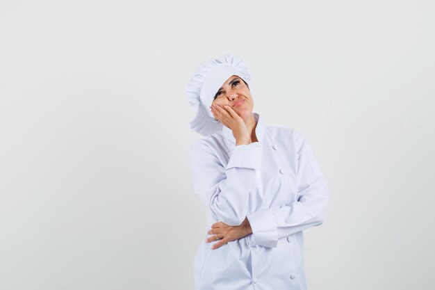 Chef mujer mirando hacia arriba en uniforme blanco y mirando pensativo