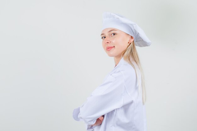 Chef mujer mirando a la cámara con los brazos cruzados en uniforme blanco y mirando confiado. vista frontal.