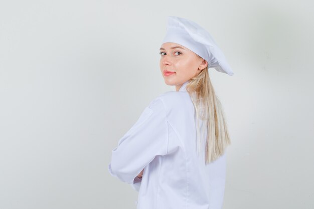 Chef mujer mirando a la cámara por encima del hombro en uniforme blanco y mirando positivo.