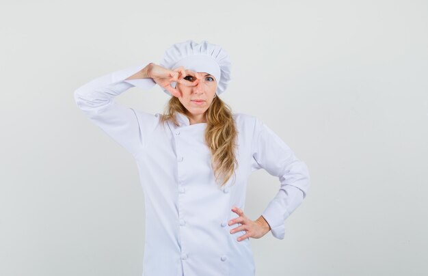 Chef mujer mirando a través de los dedos en uniforme blanco