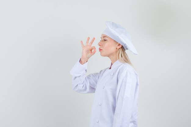 Chef mujer mostrando delicioso gesto en uniforme blanco y mirando orgulloso