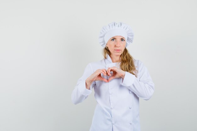 Chef mujer mostrando gesto de corazón en uniforme blanco y mirando positivo