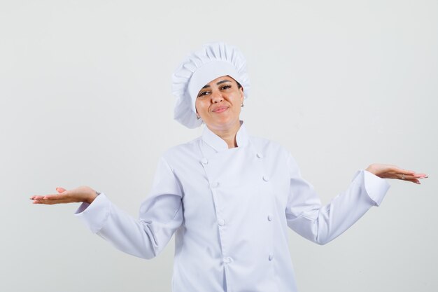 Chef mujer mostrando gesto de escalas en uniforme blanco y mirando confundido.