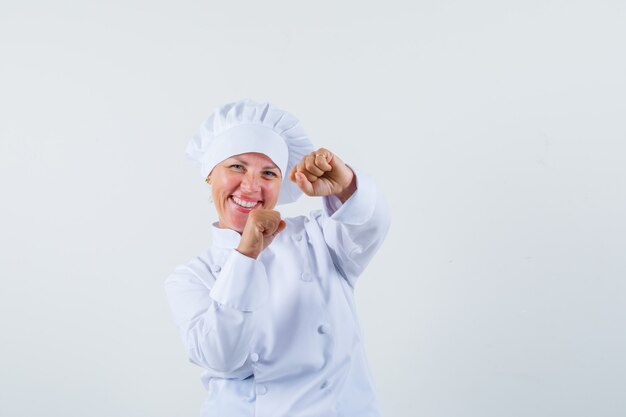 Foto gratuita chef mujer mostrando gesto ganador en uniforme blanco y mirando alegre