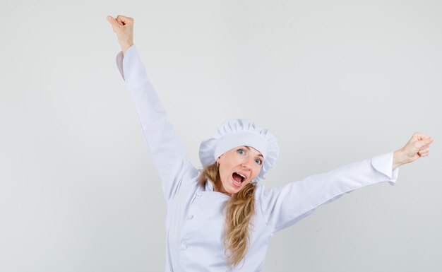 Chef mujer mostrando gesto ganador en uniforme blanco y mirando feliz