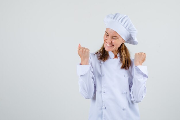 Chef mujer mostrando gesto ganador en uniforme blanco y mirando feliz