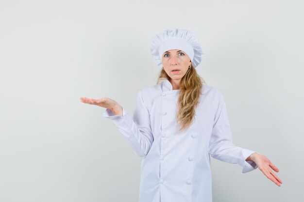 Chef mujer mostrando gesto de impotencia en uniforme blanco y mirando desconcertado