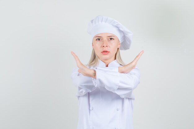 Chef mujer mostrando gesto de parada en uniforme blanco y mirando serio