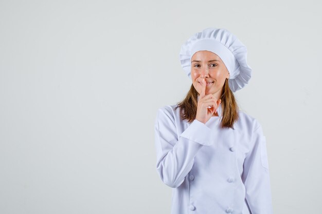 Chef mujer mostrando gesto de silencio y sonriendo en uniforme blanco