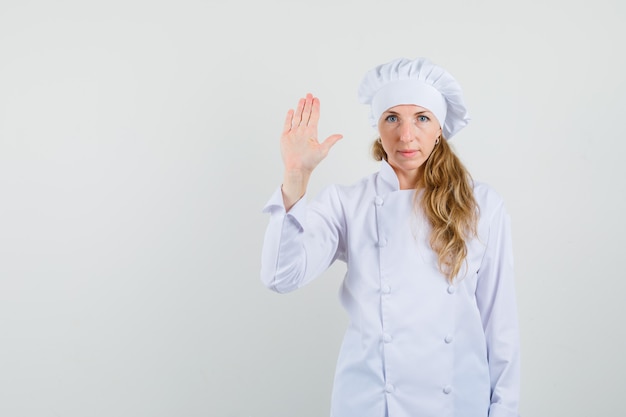 Chef mujer mostrando la palma para saludar en uniforme blanco y mirando tranquilo