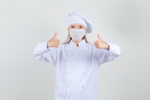 Chef mujer mostrando los pulgares para arriba en uniforme blanco y mirando complacido