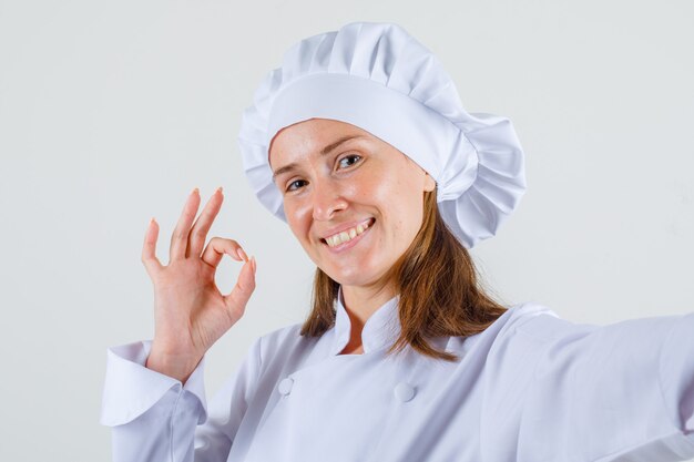 Chef mujer mostrando signo ok en uniforme blanco y mirando contento