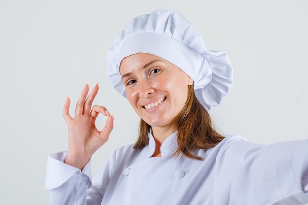 Chef mujer mostrando signo ok en uniforme blanco y mirando contento