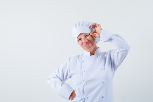 Chef mujer pellizcando su párpado en uniforme blanco y luciendo raro