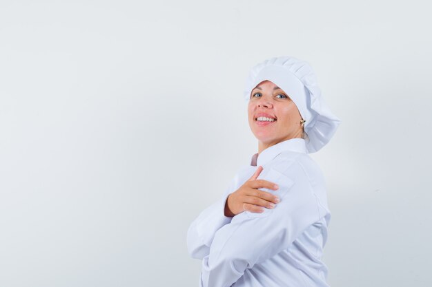 Chef mujer de pie con los brazos cruzados en uniforme blanco y mirando confiado