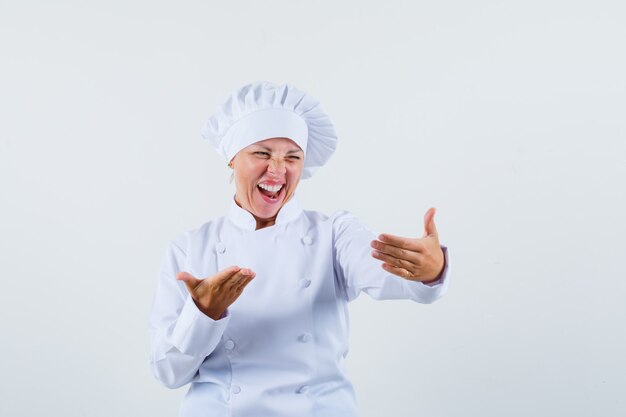 Chef mujer posando como riendo mientras mira el teléfono en uniforme blanco y mirando divertido