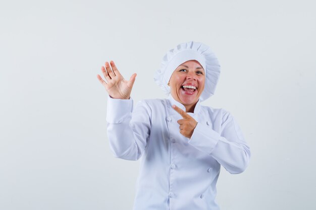Chef mujer posando como señalando algo en su mano con uniforme blanco y mirando contento