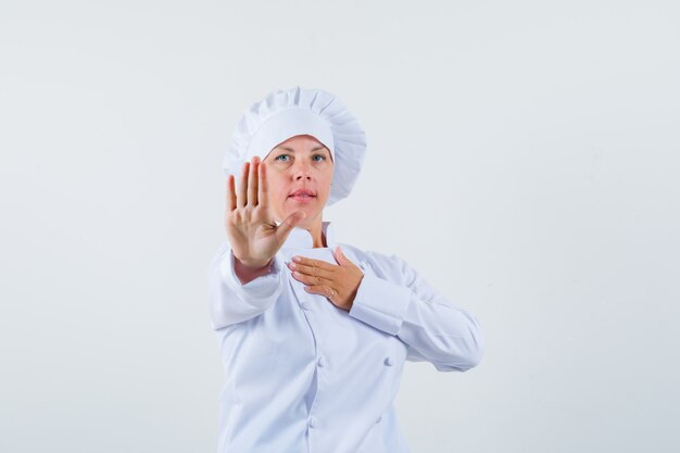 Chef mujer rechazando algo en uniforme blanco y mirando reacio