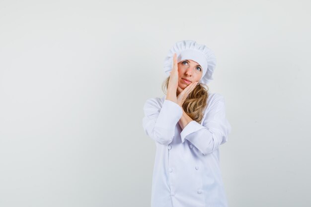 Chef mujer revisando la piel de su rostro mientras mira hacia arriba en uniforme blanco y se ve linda.